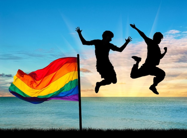 Pojęcie osób homoseksualnych. sylwetka dwóch szczęśliwych gejów skacze z flagą o zachodzie słońca