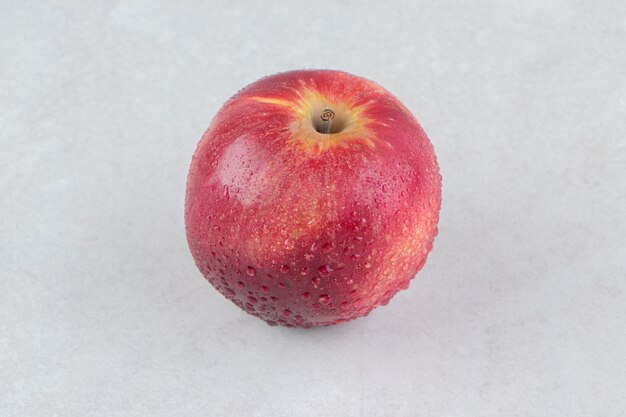 Pojedyncze czerwone jabłko na kamiennym stole.