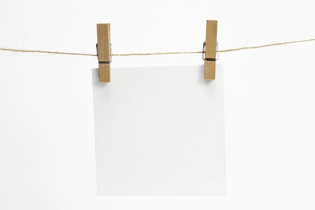 Bezpłatne zdjęcie pojedynczy pusty arkusz papieru na notatki wiszące na linie z spinaczami do bielizny i odizolowane na białym.