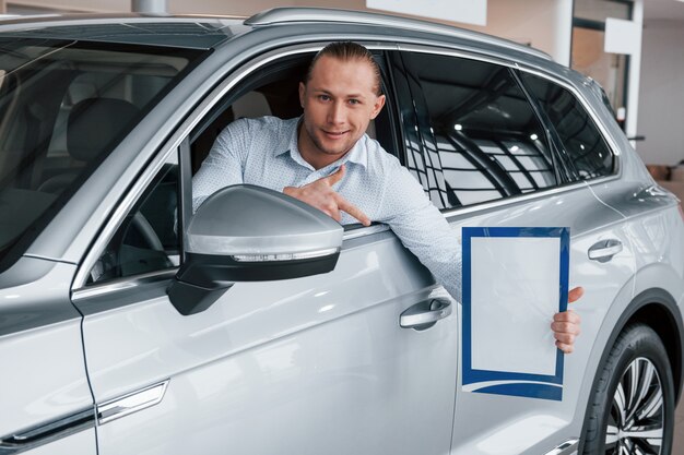 Pokazywanie palcem wskazującym. Kierownik siedzi w nowoczesnym białym samochodzie z papierem i dokumentami w ręce