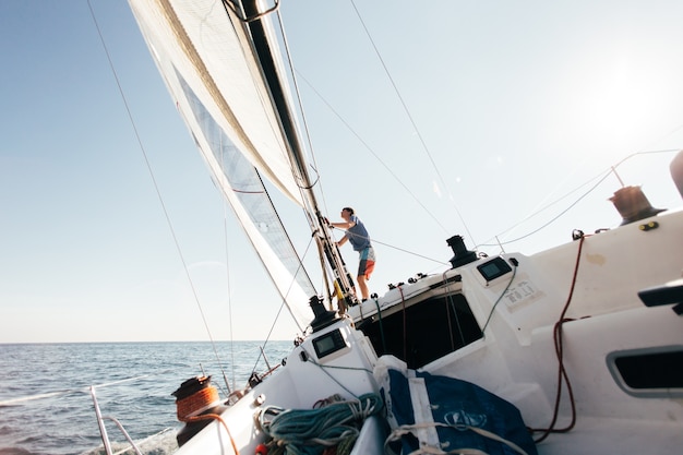 Bezpłatne zdjęcie pokład profesjonalnej żaglówki lub jachtu regatowego podczas zawodów w słoneczny i wietrzny letni dzień, szybko poruszający się przez fale i wodę, ze spinakerem w górę