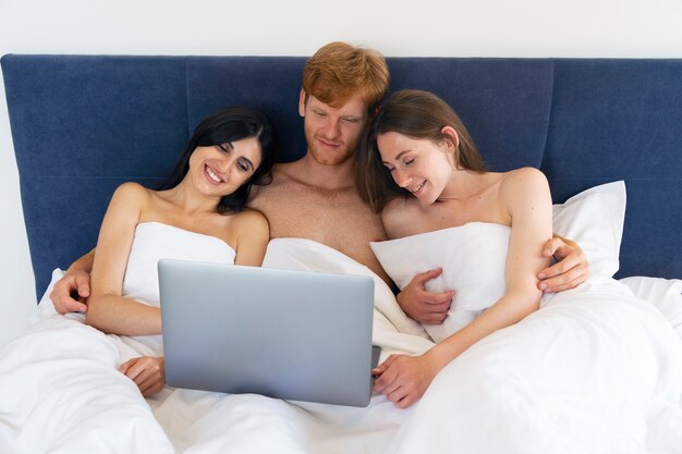 Poliamoryczna para w domu w łóżku z laptopem