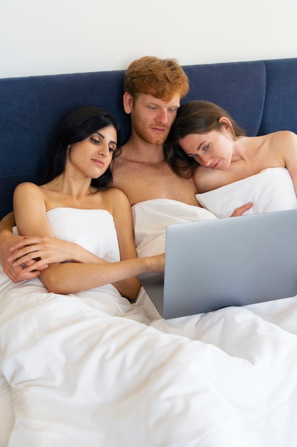 Poliamoryczna para w domu w łóżku z laptopem