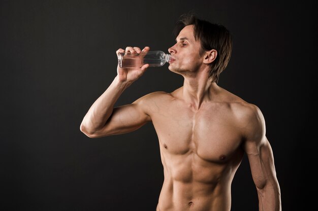 Półnagi lekkoatletycznego mężczyzna pije z butelki z wodą