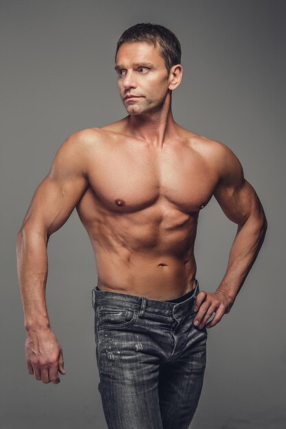 Półnagi muskularny mężczyzna w średnim wieku w dżinsach pozowanie Studio na szarym tle.