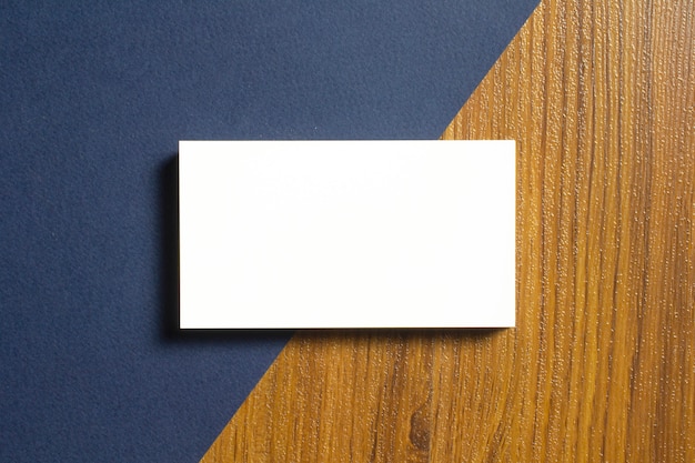 Połowa pustych wizytówek leży na niebieskim papierze z fakturą i drewnianym biurku