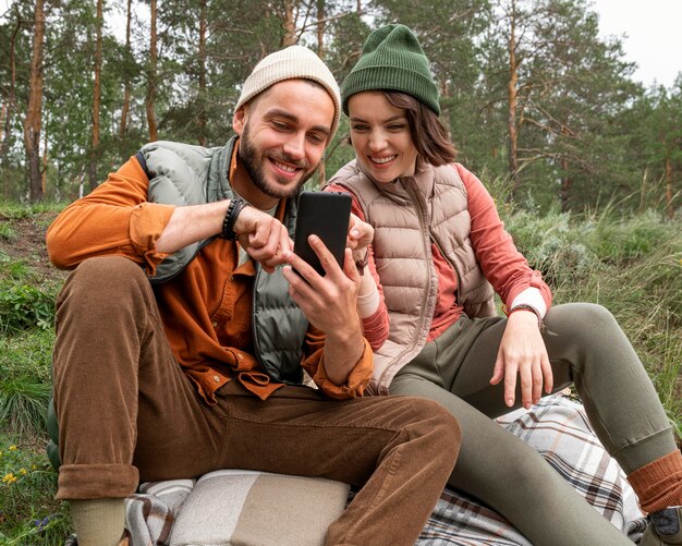 Połowa strzału para siedzi na trawie i patrząc na telefon