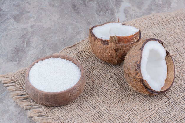 Połowę pokroić orzechy kokosowe i miskę cukru na tle kamienia.