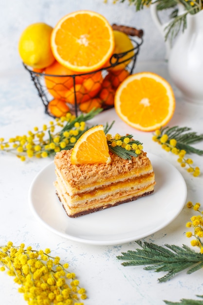 Pomarańczowe ciasto ozdobione świeżymi pomarańczowymi plasterkami i kwiatami mimozy na świetle