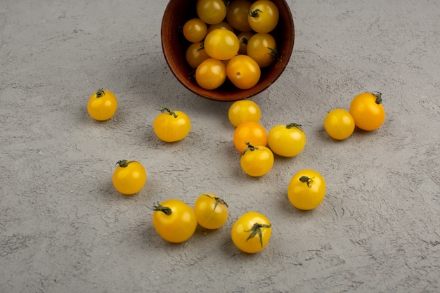 Pomidory żółte dojrzałe świeże wewnątrz i na zewnątrz brązowej okrągłej doniczki na szaro