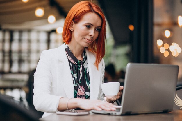 Pomyślna biznesowa kobieta pracuje na laptopie w kawiarni