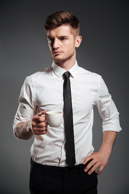 Pomyślny biznesmen trzyma filiżankę kawy w formalwear podczas gdy stojący