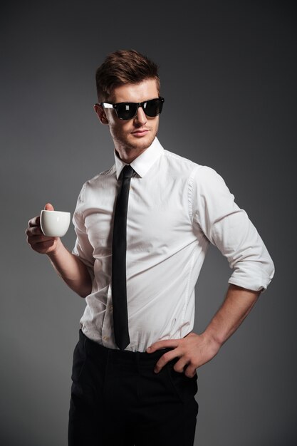 Pomyślny biznesmen trzyma filiżankę kawy w formalwear podczas gdy stojący