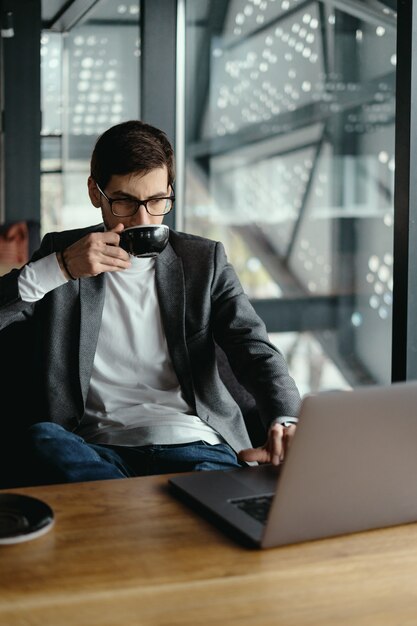 Pomyślny biznesowy mężczyzna pracuje na laptopie podczas gdy pijący kawę