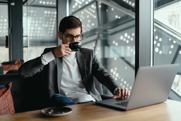 Pomyślny biznesowy mężczyzna pracuje na laptopie podczas gdy pijący kawę