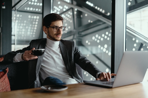 Pomyślny biznesowy mężczyzna pracuje na laptopie podczas gdy pijący kawę