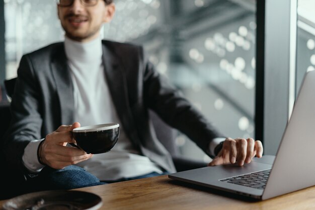 Pomyślny biznesowy mężczyzna pracuje na laptopie podczas gdy pijący kawę