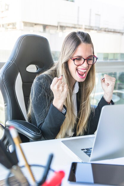 Pomyślny młody bizneswoman patrzeje laptop zaciska jej pięść