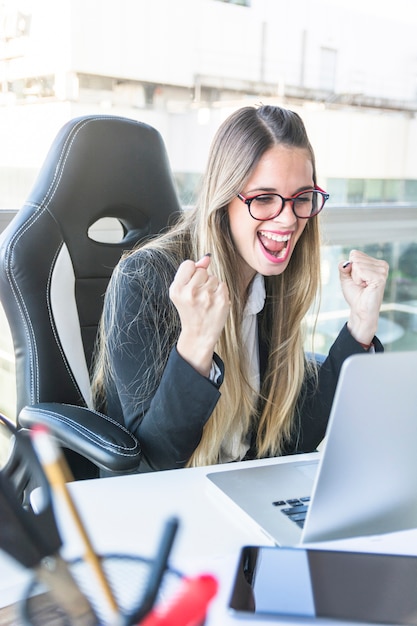 Pomyślny młody bizneswoman patrzeje laptop zaciska jej pięść