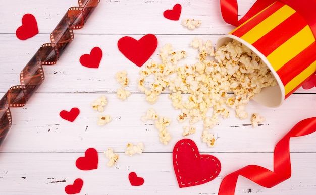 Popcorn, czerwone serca i wstążki na białym tle drewnianych. walentynki, kino.