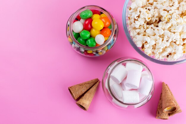 Popcorn i pianki marshmallows z widokiem z góry wraz z kolorowymi cukierkami na różowym, kolorowym cukrze lizakowym