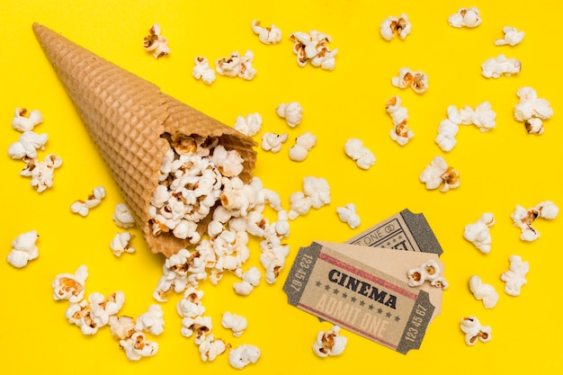 Bezpłatne zdjęcie popcorn wylewający się z rożka waflowego z biletami do kina na żółtym tle