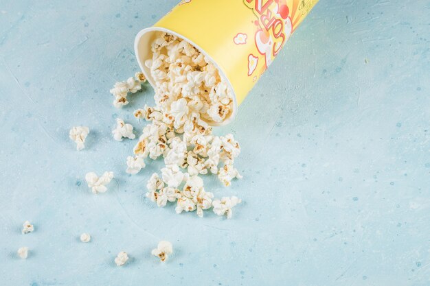 Popcorny z żółtego pojemnika na niebieskim stole