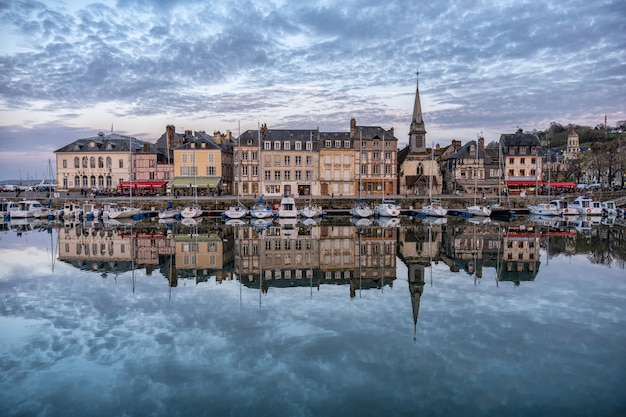 Port Honfleur z budynkami odbijającymi się w wodzie pod zachmurzonym niebem we Francji