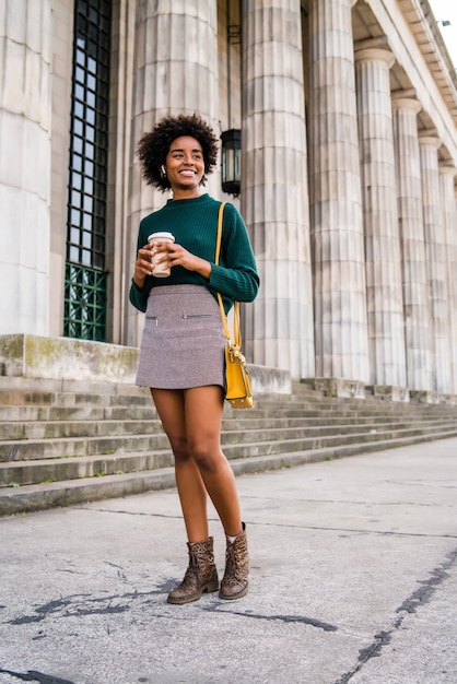 Portret afro bizneswoman trzyma filiżankę kawy podczas spaceru na ulicy na ulicy. Koncepcja biznesowa i miejska.