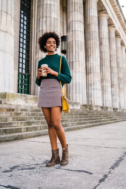 Portret afro bizneswoman trzyma filiżankę kawy podczas spaceru na ulicy na ulicy. Koncepcja biznesowa i miejska.