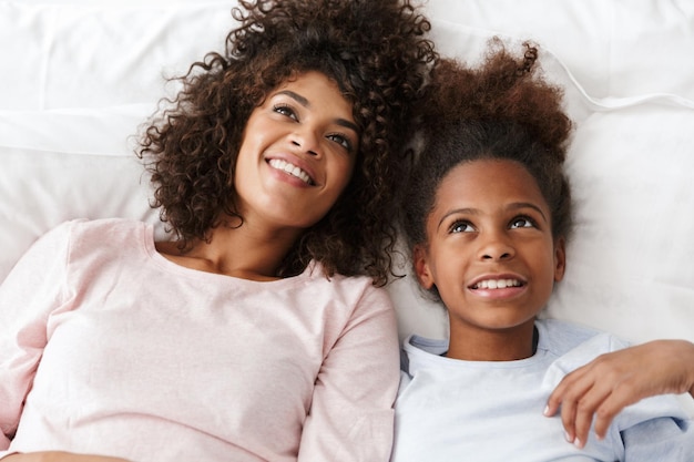 Portret afroamerykanki i jej córki uśmiechniętej i leżącej w łóżku w domu