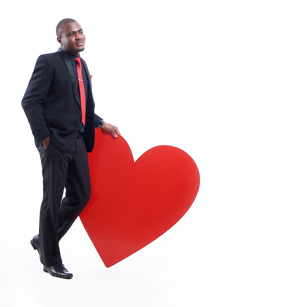 Portret afrykańskiego biznesmena w czarnym apartamencie i czerwonym krawacie, pozowanie i opierając się wielkim czerwonym sercem.