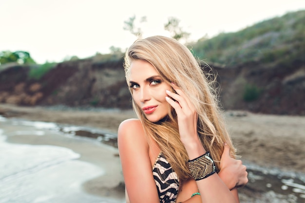 Portret atrakcyjna blondynka z długimi włosami, pozowanie na kamienistej plaży. Ona patrzy w kamerę.