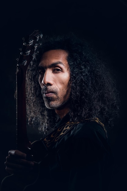 Portret atrakcyjne kręcone mężczyzna z gitarą w ciemnym studio fotograficznym.