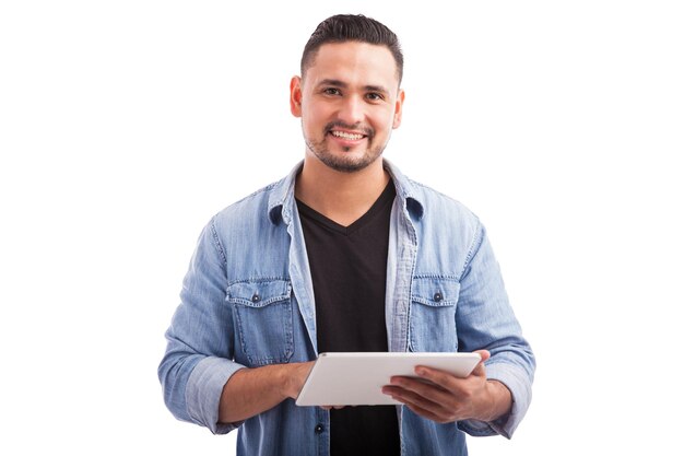 Portret atrakcyjnego młodego mężczyzny ubranego swobodnie, korzystającego z komputera typu tablet i uśmiechającego się na białym tle