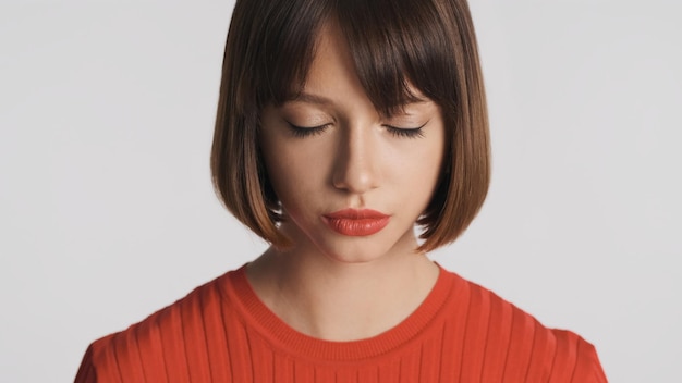 Portret atrakcyjnej brunetki dziewczyny z bobowymi włosami i czerwonymi ustami marzycielsko zamykającymi oczy na białym tle