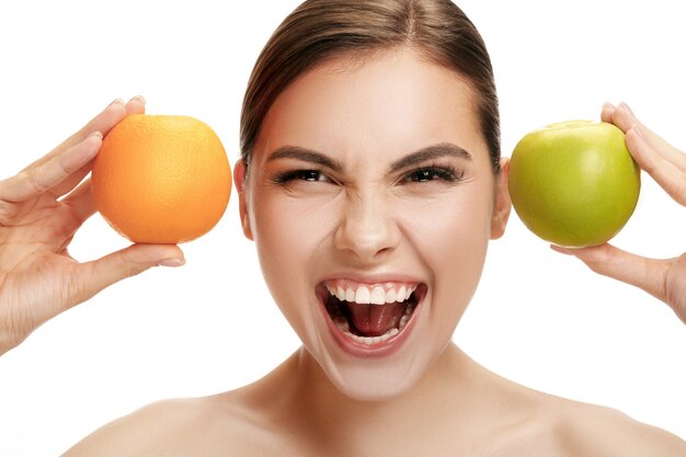 Portret atrakcyjnej kaukaskiej uśmiechniętej kobiety na białym tle studio z zielonym jabłkiem i pomarańczowymi owocami