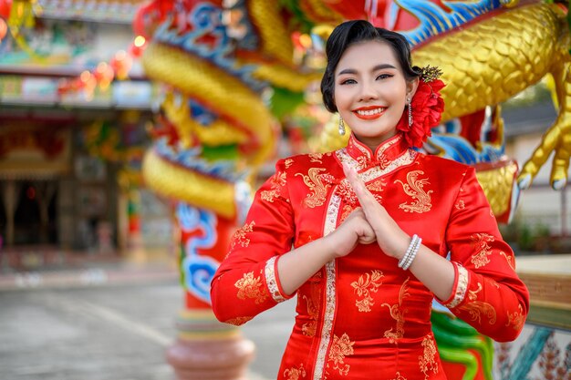 Portret Azjatycka piękna kobieta ubrana w cheongsam uśmiechnięta i pozuje z gestem gratulacji w świątyni na chiński nowy rok