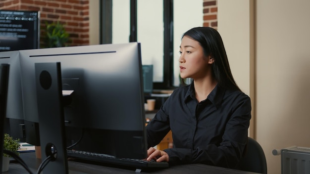 Portret azjatyckiego programisty skupionego na pisaniu kodu siedzącego przy biurku w biurze rozwoju oprogramowania. Inżynier systemowy koncentrujący się na stworzeniu algorytmu dla tego startupu.