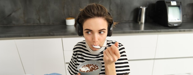 Bezpłatne zdjęcie portret beztroskiej brunetki jedzącej płatki, słuchającej muzyki, śniadającej w
