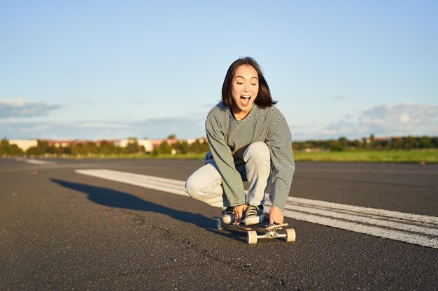 Portret beztroskiej szczęśliwej azjatyckiej dziewczyny jeżdżącej na deskorolce i śmiejącej się, ciesząc się słonecznym dniem