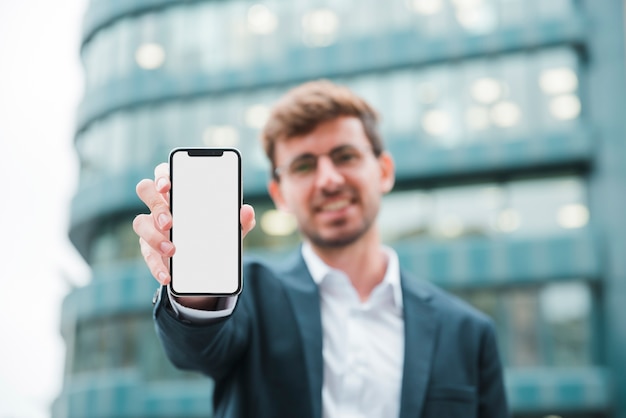 Portret biznesmen stoi przed budynkiem pokazuje telefon komórkowego