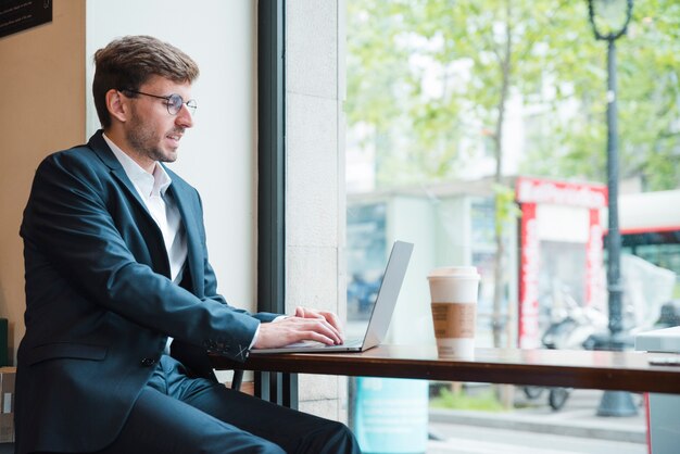 Portret biznesmen używa laptop z takeaway filiżanką na stole w kawiarni