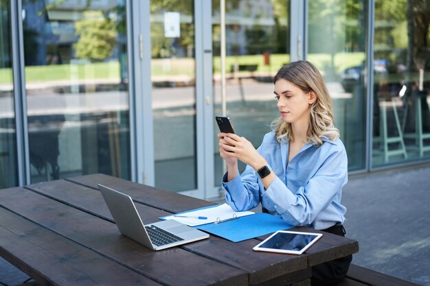 Portret bizneswoman siedzącej na zewnątrz i pracującej młodej korporacyjnej kobiety patrzącej na jej smartpho