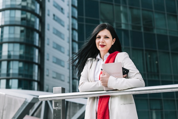 Bezpłatne zdjęcie portret bizneswomanu mienia telefon komórkowy z budynkiem w tle i dzienniczek