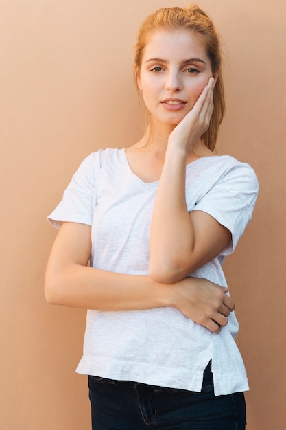 Bezpłatne zdjęcie portret blondynki młoda kobieta patrzeje kamerę z jej rękami na podbródku