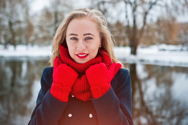 Portret blondynki w czerwonym szaliku i płaszczu przed zamarzniętym jeziorem w zimowy dzień