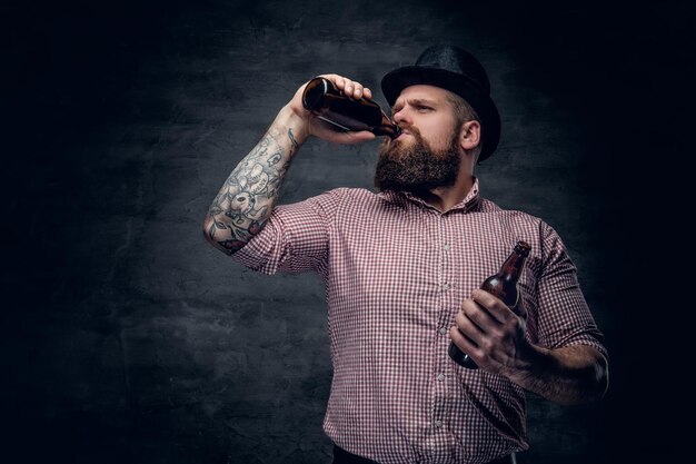 Portret brodatego mężczyzny w koszuli w kratę i cylindrycznym kapeluszu, pijącego piwo z butelki.