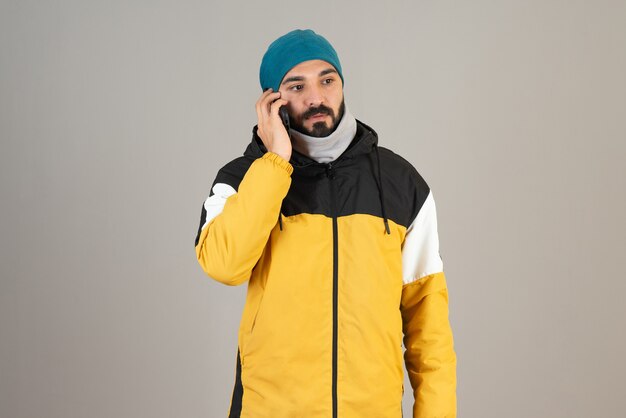 Portret brodaty mężczyzna w ciepłych ubraniach rozmawia przez telefon komórkowy.
