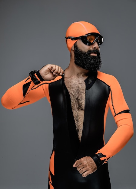 Bezpłatne zdjęcie portret brodaty mężczyzna w masce do nurkowania i pomarańczowym neoprenowym kombinezonie do nurkowania na białym tle na szarym tle.